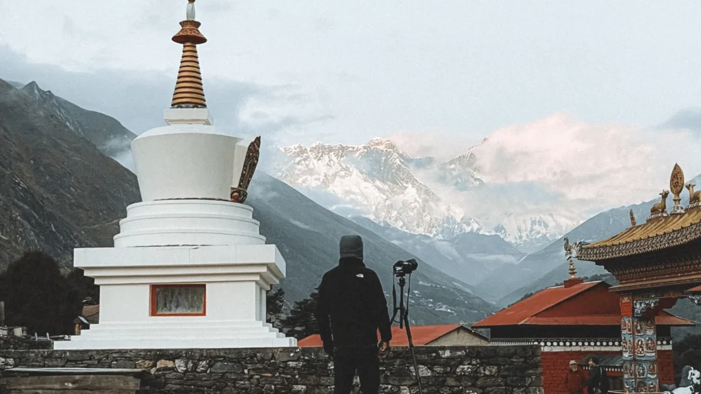 hotography adventure in Nepal setting up a tripod beside a white stupa, with snow-capped Everest region peaks in the background